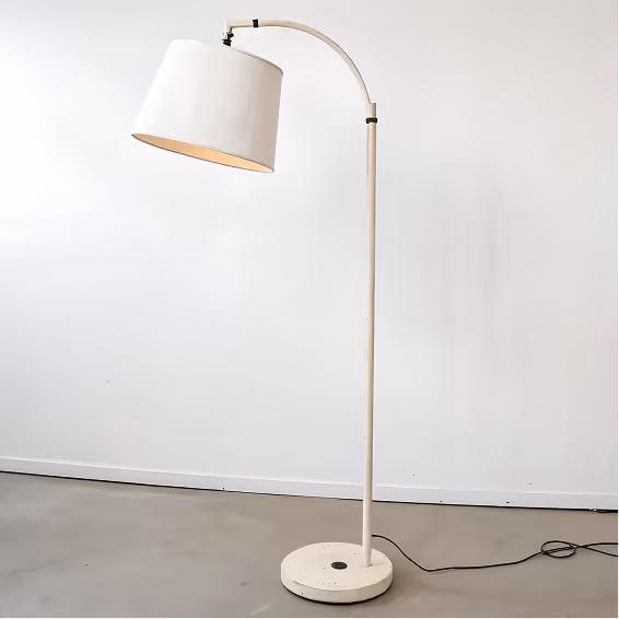 Minimalist white arc floor lamp with a round base and tilted drum shade against a plain white wall.