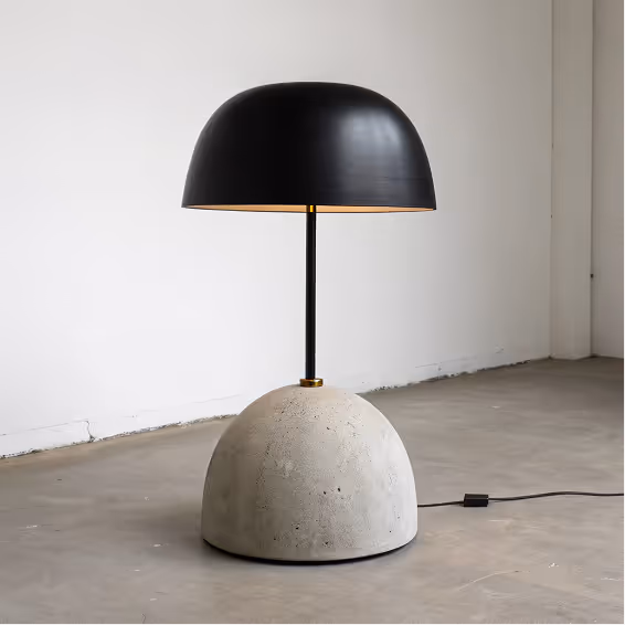 Modern floor lamp with a black dome-shaped shade and a rounded concrete base on a gray floor.