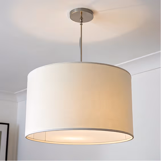 Modern ceiling pendant light with a large white fabric drum shade in a room with white walls.