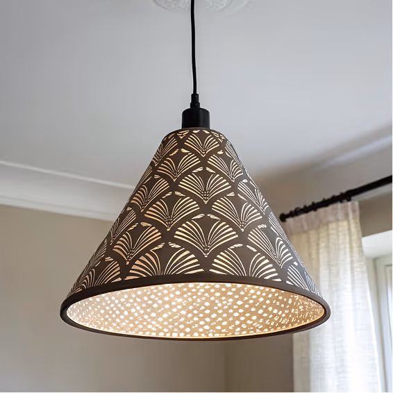 Conical pendant lamp with decorative cutout pattern emitting warm light in a room with beige walls and white curtains.